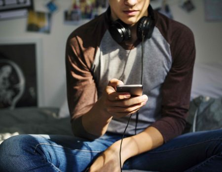 Teenage boy in a bedroom listening to music through his smartphone
